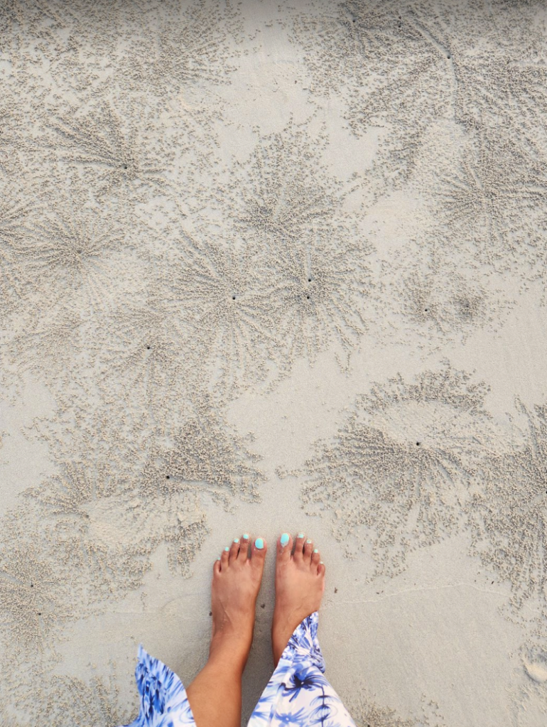 womans feet on a sandy beach with patterns made by crabs digging holes