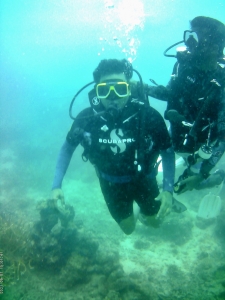 man in scuba diving gear under water with a trainer also in gear behind him