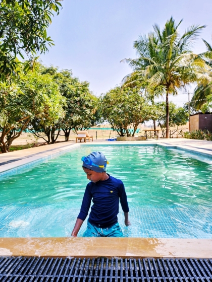 child in swimming gear at the edge of a small swimming pool surrounded by trees