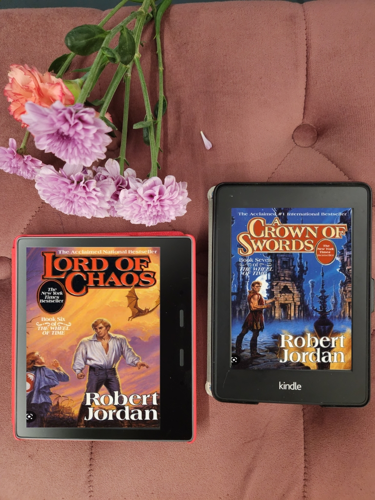 Robert Jordan's Wheel of Time Book 6 and 7 Lord of Chaos and Crown of Swords on Kindle Oasis and Kindle Paperwhite on a pink cushion with flower stems on top