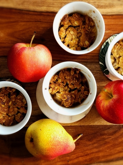 Apples and pears with 4 cups of apple crumble set on a wooden table